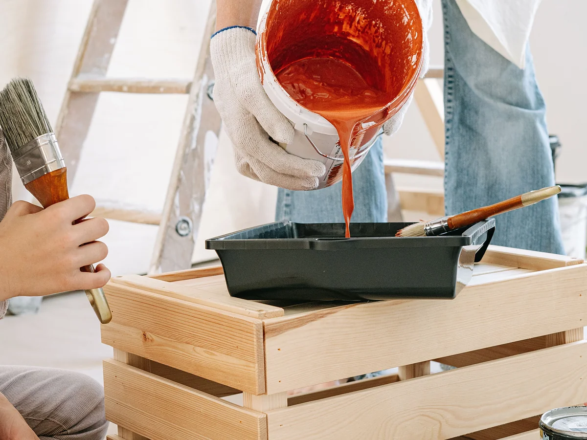 Gloved hands pouring paint into a roller tray before painting a room